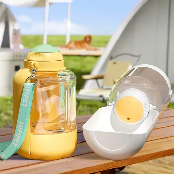 6fc352a4-9ac8-456b-84e3-fcbe7796989c.jpg Outdoor product photo: yellow baby bottle with teal hip strap beside a white bottle warmer on a wooden table; dog in the blurred background